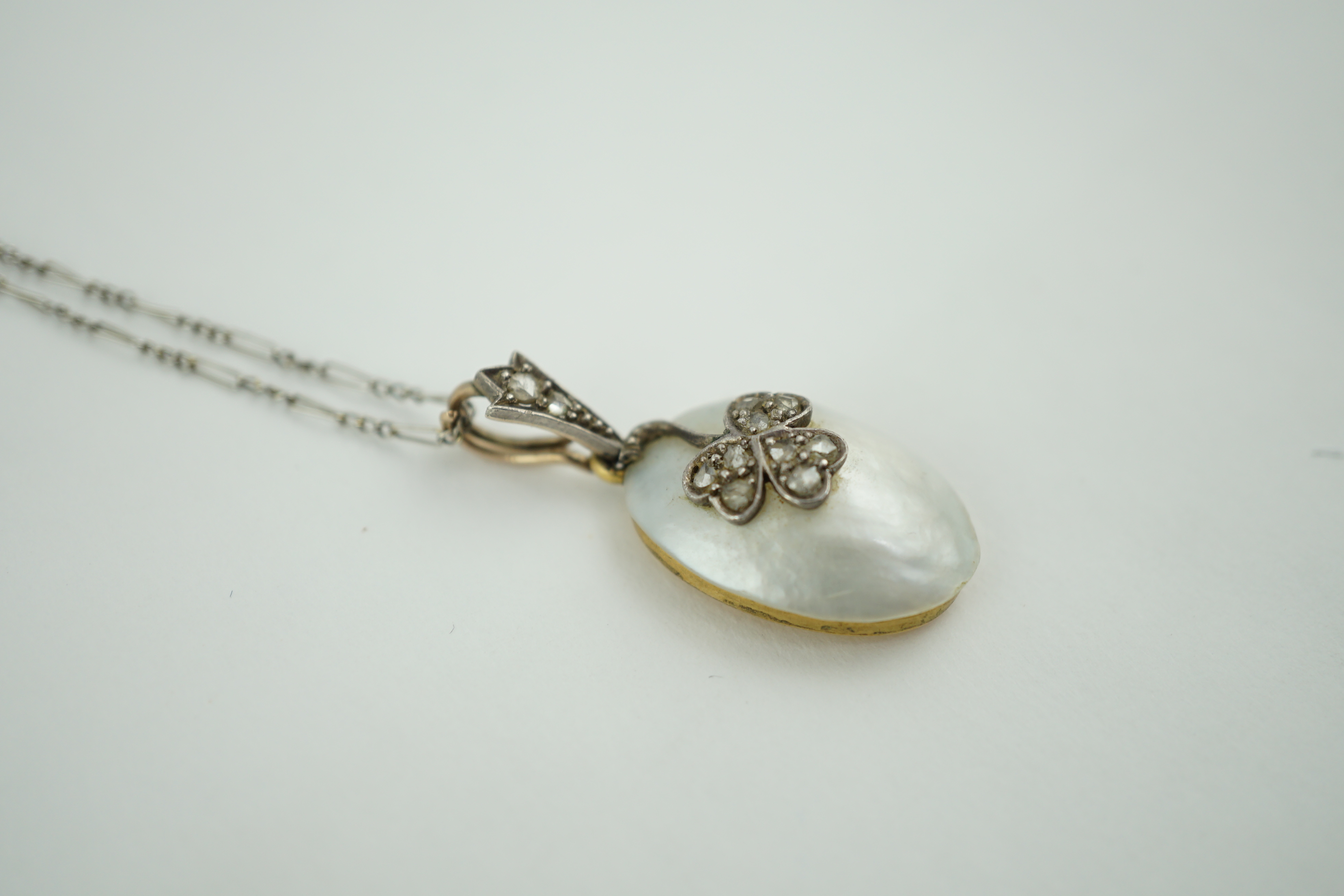 A 1920's gold and mabe pearl set oval pendant, with rose cut diamond set floral motif, on a platinum chain